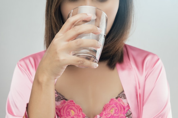 Mujeres asiáticas en camisón de satén rosa bebiendo agua.