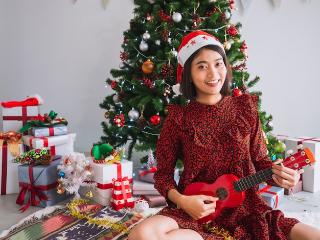 Las mujeres asiáticas celebran la Navidad tocando la guitarra en casa, una niña toca una canción con una sonrisa el día de Navidad