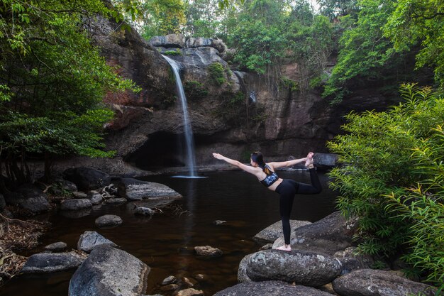 Las mujeres asiáticas de la chica joven están jugando a yoga delante de la cascada