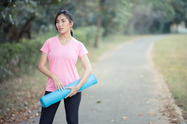 Las mujeres asiáticas con colchonetas de yoga van a hacer yoga en el parque para mantenerse saludables y en buena forma.