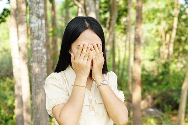 Las mujeres asiáticas se cubren los ojos con ambas manos en el fondo de la naturaleza