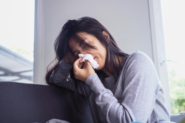 Las mujeres asiáticas están enfermas con secreción nasal y resfriados Mujer joven enferma cubierta con una manta y estornudos Concepto de mujer enferma