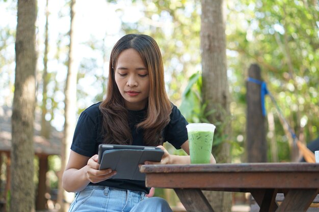 Las mujeres asiáticas están felices de sentarse y trabajar en una cafetería. Hay árboles verdes rodeados de naturaleza. La planificación empresarial es una buena idea.