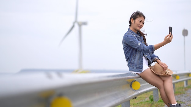 Las mujeres asiáticas están fotografiando autofotos desde un teléfono móvil, con el fondo como una turbina eólica y un prado