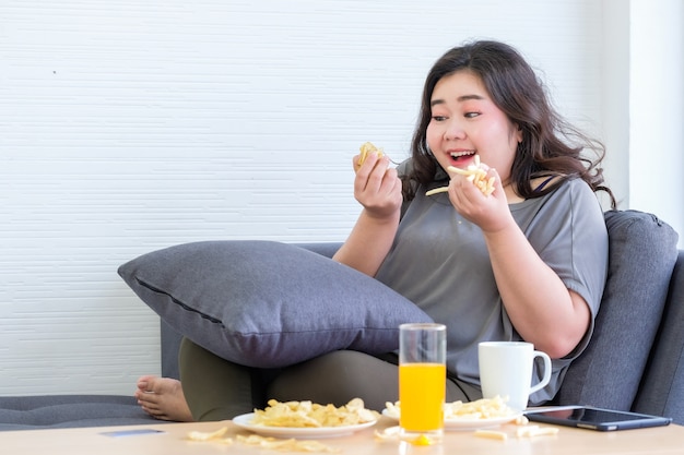 Las mujeres asiáticas gordas disfrutan comiendo papas fritas en la habitación.