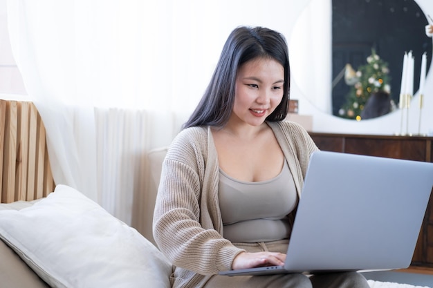 Mujeres asiáticas jóvenes y atractivas con ropa acogedora usando una laptop en la cama en casa, tiempo de Navidad