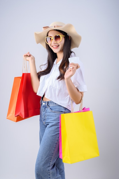 Las mujeres asiáticas jóvenes con gafas y sombreros sostiene la cuenta con muchas bolsas de colores sobre fondo blanco.