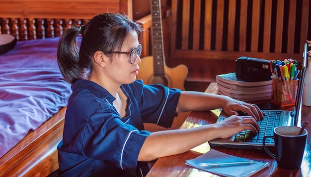 Mujeres asiáticas jóvenes o negocios de mujeres Trabajando Siéntate en casa con una computadora portátil en una mesa de madera