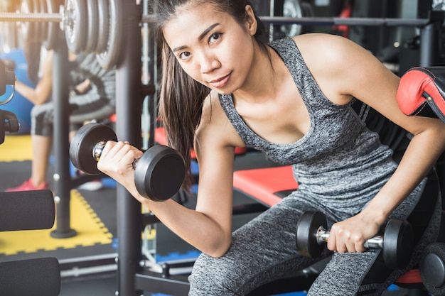 Mujeres asiáticas jovenes que levantan pesas de gimnasia en gimnasio de deporte