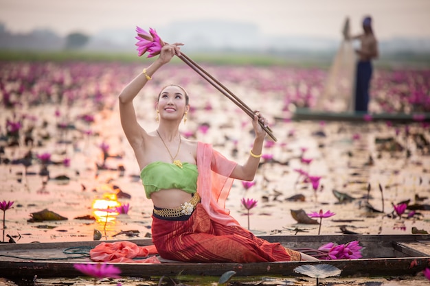 Mujeres asiáticas jóvenes en traje tradicional en el barco y flores de loto rosa en el estanque. Hermosas chicas en traje tradicional. Cultural