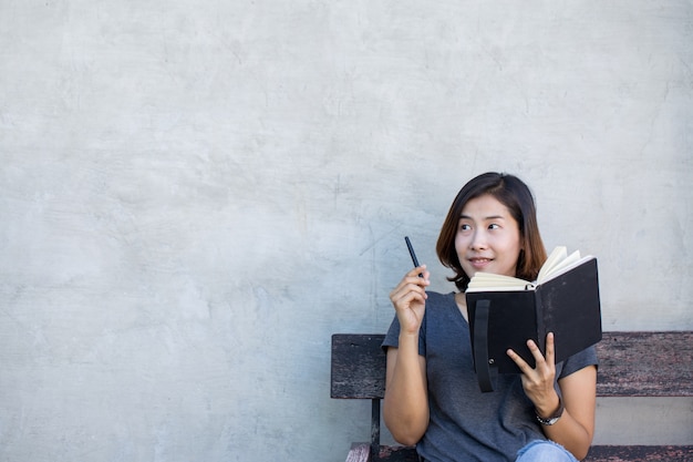 Las mujeres asiáticas lindas están pensando algo con su libro sobre fondo gris