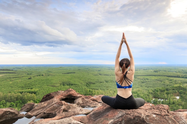 Las mujeres asiáticas lo juegan yoga en el acantilado de la roca de la montaña.