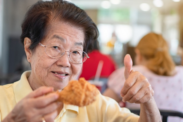 Las mujeres asiáticas mayores están comiendo pollo frito. En el restaurante Y levanta el pulgar.