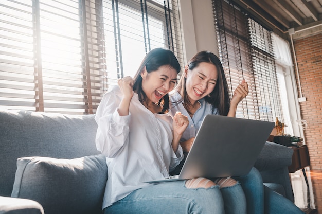 Las mujeres asiáticas mejores amigas emocionados mientras usan la computadora portátil en casa