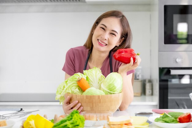 Las mujeres asiáticas que cocinan ensalada de verduras orgánicas comen saludable en la cocina de casa