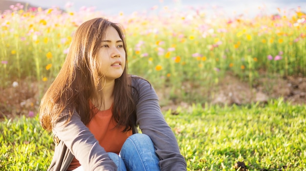 Mujeres asiáticas que se sientan en el jardín de flores del cosmos.