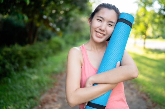 Las mujeres asiáticas que sostienen colchonetas de yoga van a hacer yoga en el parque para mantenerse saludables y en buena forma.