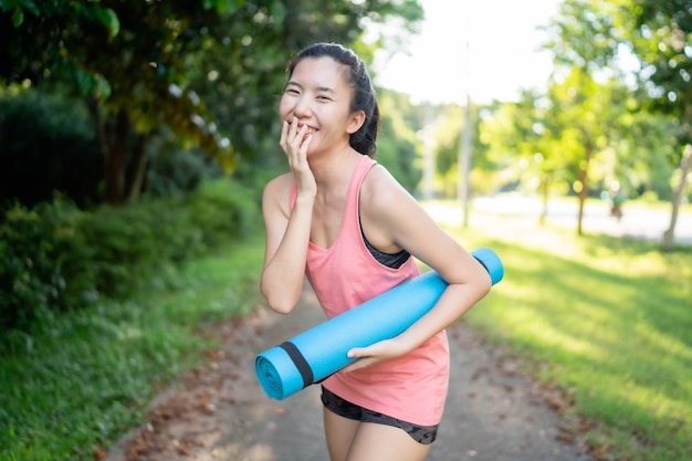 Las mujeres asiáticas que sostienen colchonetas de yoga van a hacer yoga en el parque para mantenerse saludables y en buena forma.