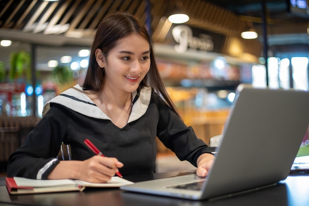 Mujeres asiáticas que trabajan y aprenden en línea con el portátil. ella sonriendo y feliz