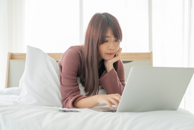 Mujeres asiáticas que trabajan con la computadora portátil en la cama