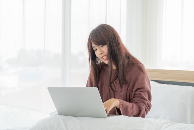 Mujeres asiáticas que trabajan con el portátil en la cama en casa