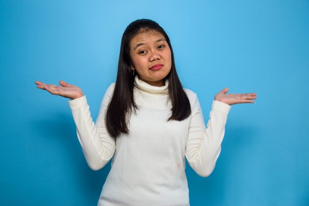 Las mujeres asiáticas que usan camiseta blanca aislada en azul miran a la cámara y hacen un gesto confuso