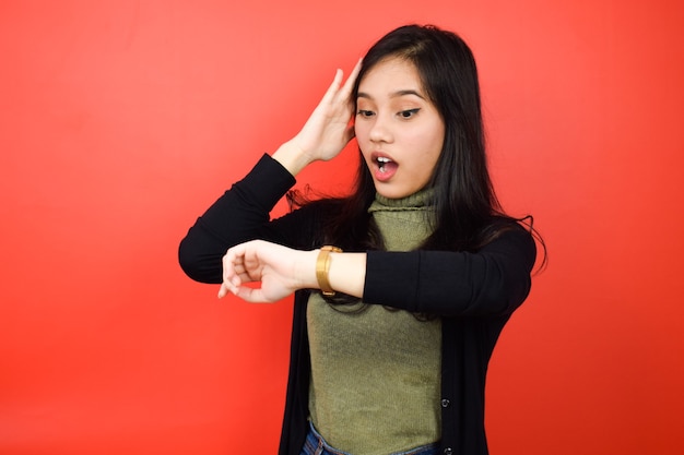 Mujeres asiáticas que usan suéter negro mirando un reloj y conmocionadas con fondo rojo aislado