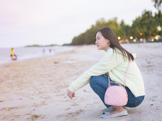 Mujeres asiáticas que viajan al mar sentadas en la playa mirando a su alrededor liberación de muestra gratis Relájese en la atmósfera Hay un bokeh de contraluz