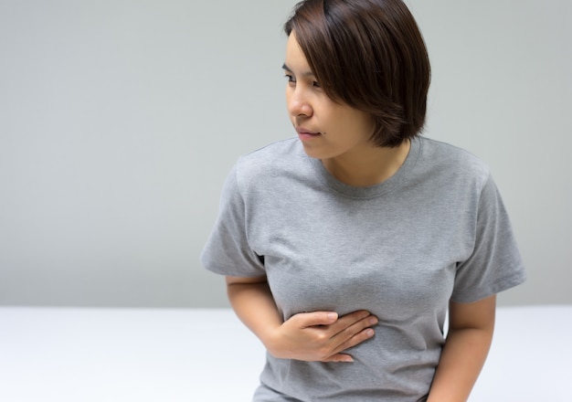 Foto mujeres asiáticas sentadas en la cama con dolor abdominal.