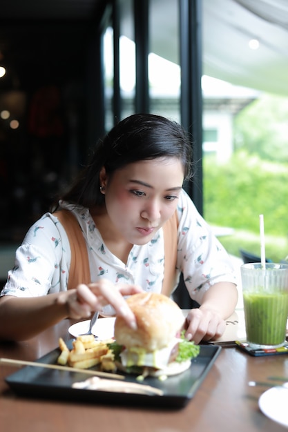 Las mujeres asiáticas sonriendo y felices y disfrutaron de comer hamburguesas en el café y el restaurante