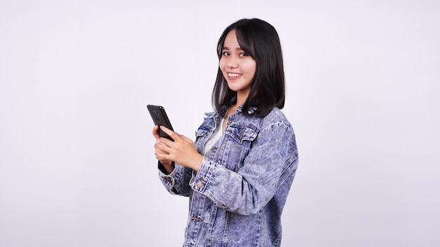 Mujeres asiáticas sonriendo vistiendo chaqueta de jeans y sosteniendo el teléfono con superficie blanca aislada