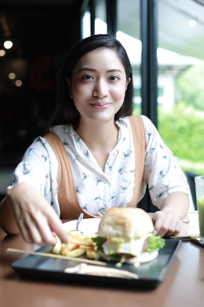 Las mujeres asiáticas sonrientes y felices y disfrutaron comiendo hamburguesas en el café y el restaurante en el momento de relajarse