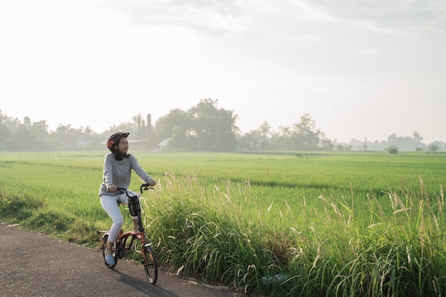 Las mujeres asiáticas usan cascos para andar en bicicleta plegable en los arrozales