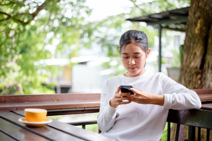 Mujeres asiáticas usando mensajes de escritura en un teléfono móvil en la cafetería