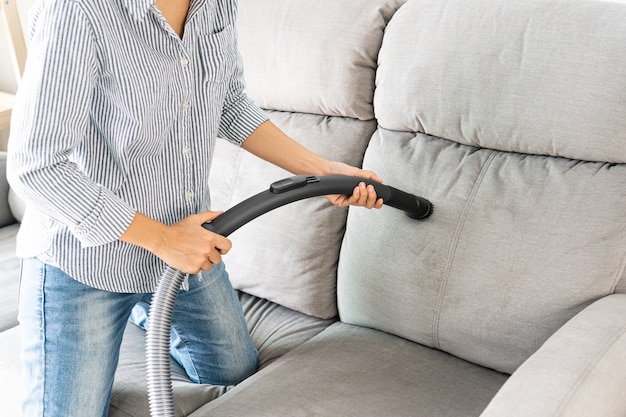 Las mujeres con aspiradora limpieza sofá en la sala de estar en casa. De cerca