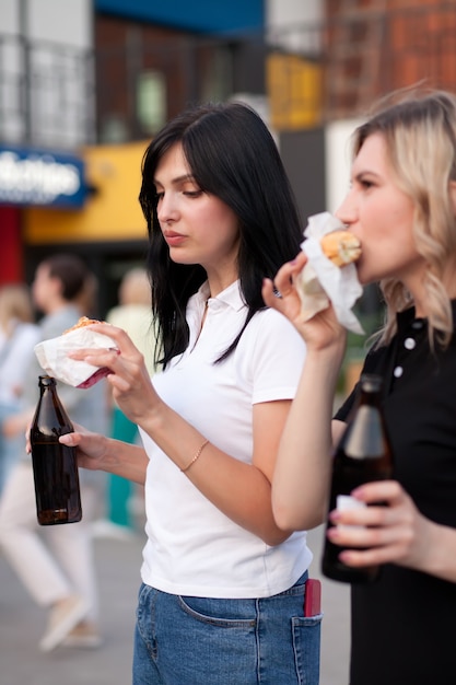 Mujeres bastante jóvenes comiendo hamburguesas al aire libre en la calle.