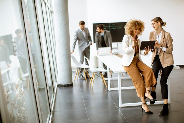 Mujeres bastante jóvenes con tableta digital en la oficina moderna frente a su equipo