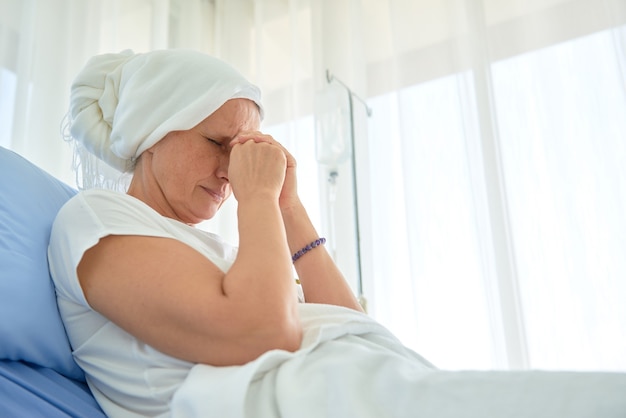 Las mujeres blancas caucásicas sin pelo y sin cejas se sienten mal están orando y esperando la quimioterapia en la habitación del hospital, concepto del mes de concientización sobre el cáncer de mama.