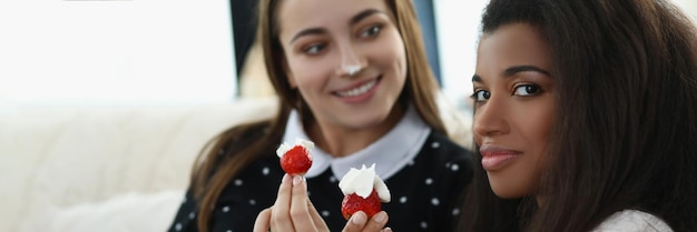 Mujeres bonitas sonrientes comiendo deliciosas fresas frescas cubiertas con crema batida