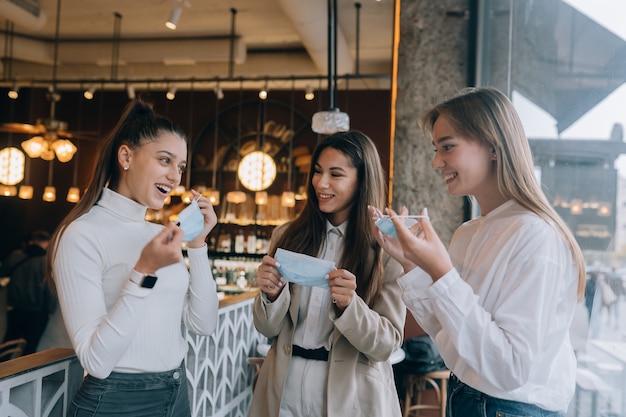 Las mujeres caucásicas quitándose una máscara médica en un café