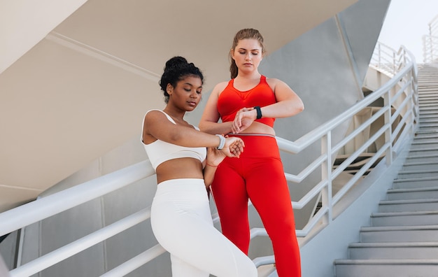Mujeres de cuerpo completo con ropa de fitness se relajan después del entrenamiento comprobando su pulso en relojes inteligentes