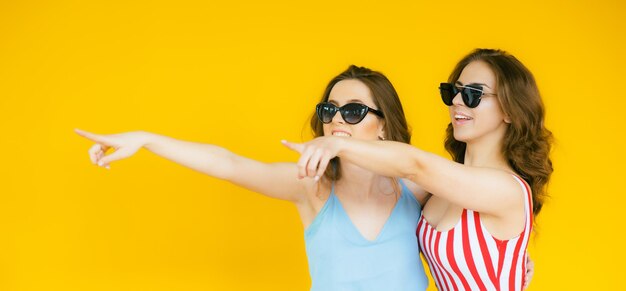 Mujeres despreocupadas sexy posando junto a la pared amarilla en gafas de sol Modelos positivos yendo