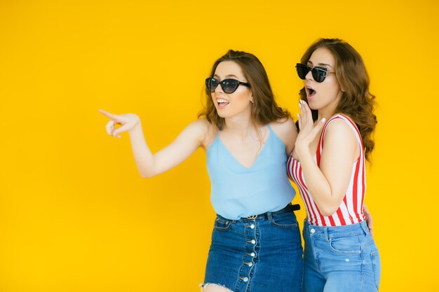 Mujeres despreocupadas sexy posando junto a la pared amarilla en gafas de sol Modelos positivos yendo