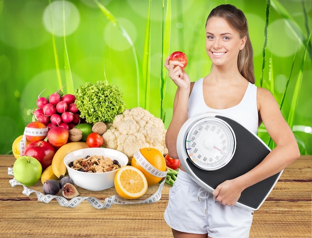 Mujeres a dieta con escala de peso, comida saludable en el fondo