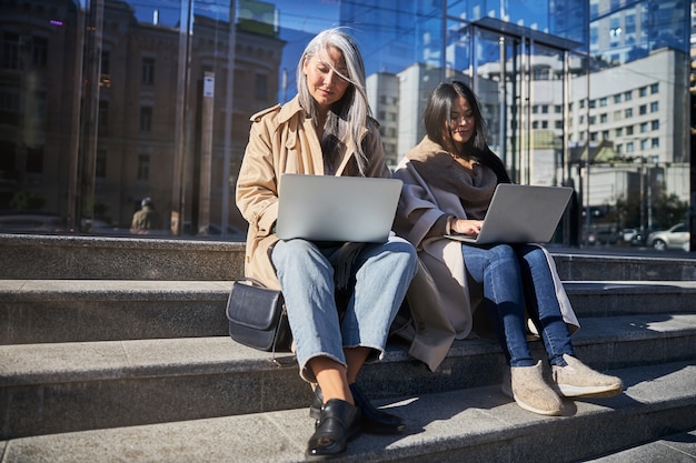 Mujeres elegantes que trabajan en ordenadores portátiles en la calle