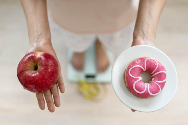 Las mujeres eligen los alimentos adecuados para una buena salud Las mujeres ayunan Opciones de comparación entre donas y manzanas durante la medición del peso en básculas digitales Concepto de dieta