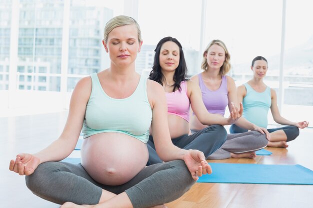 Mujeres embarazadas en clase de yoga sentado en esteras con los ojos cerrados