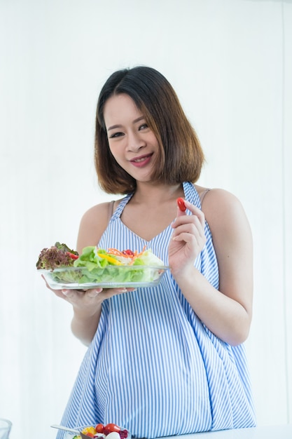 Foto mujeres embarazadas ponte un vestido azul. ella come una ensalada de vegetales