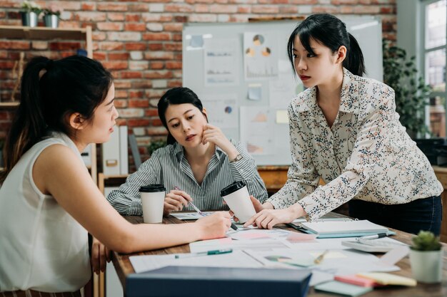 mujeres emprendedoras discutiendo en una reunión en una oficina ecológica. Gerente de mujer insatisfecha regañando a empleado por mal trabajo en grupo. líder de la dama enojada señala el documento y sostiene la taza de café