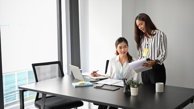 Mujeres empresarias encantadoras trabajan y discuten sus planes de negocios. Una empleada explica y muestra a su colega el documento de resultados en su oficina.